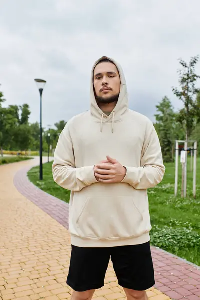 Joven en una sudadera con capucha se para con confianza, preparándose para su entrenamiento en un exuberante entorno al aire libre. - foto de stock