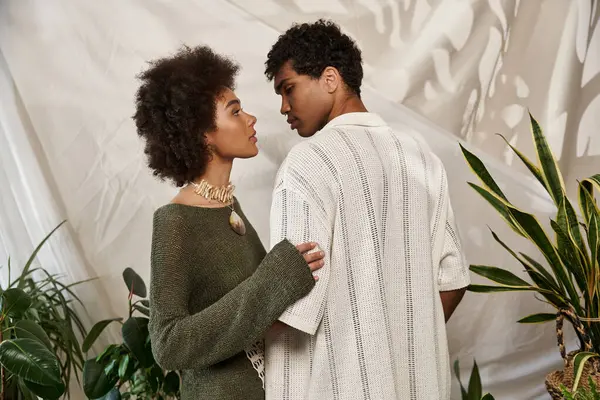 A stylish couple stands close together, surrounded by greenery, exuding love and connection. — Stock Photo