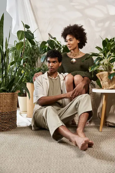 Stylish young couple shares a loving embrace amidst lush plants in a cozy indoor space. — Stock Photo