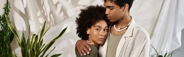 A stylish couple embraces intimately amidst a backdrop of greenery and soft fabrics, radiating love. — Stock Photo