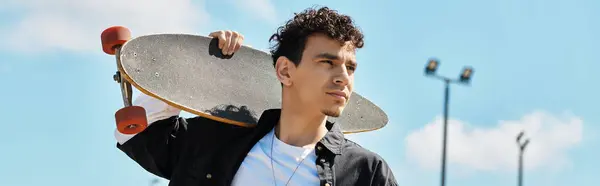 Un joven en el parque sostiene un monopatín y mira a lo lejos. — Stock Photo