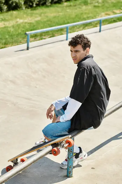A young man sits on a railing, skateboard beside him, soaking in the vibrant atmosphere of the park. — Stock Photo