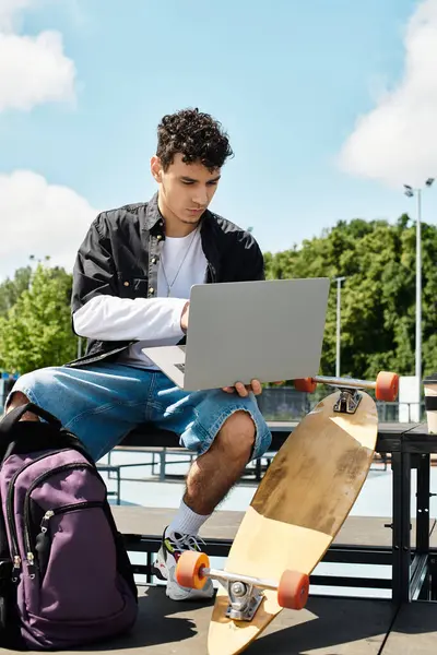 A young man sits outdoors in a park, focused on his laptop while surrounded by nature. — Stock Photo