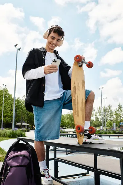 A young man on a park bench smiles at his phone, skateboard by his side under the sun. — Stock Photo