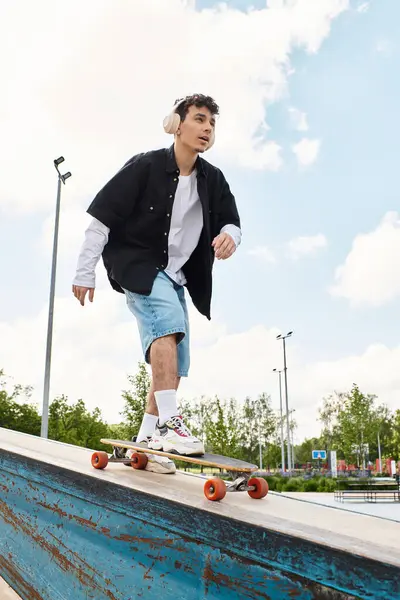 A young man rides a skateboard with headphones on, gliding smoothly at the park. — Stock Photo