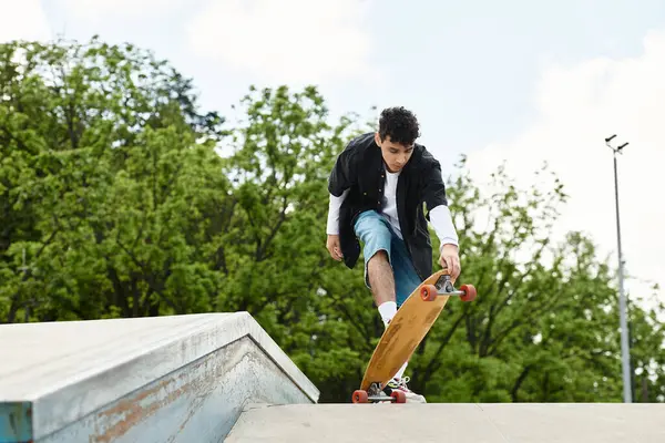 A young man expertly balances on a skateboard while navigating a ramp in a green park. — Stock Photo