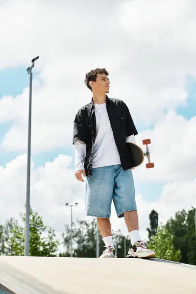 A young man in casual wear ponders his next skateboarding move in the park. — Stock Photo