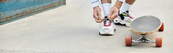 A young man prepares to skate by tying his shoelaces beside his skateboard on a warm day. — Stock Photo
