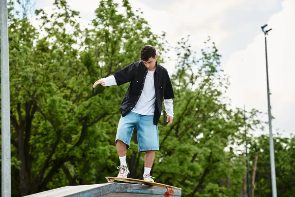 Young man balances on a skateboard at a park, demonstrating his skills among tall trees. — Stock Photo
