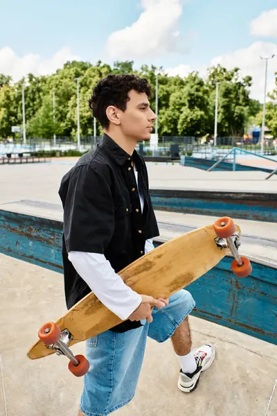 A young man stands with his skateboard in a sunny, vibrant park. — Stock Photo