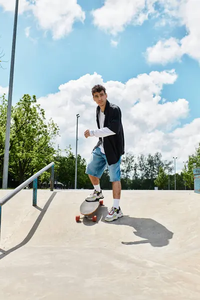 A young man skillfully skateboards in the park under a bright blue sky with clouds. — Stock Photo