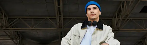 A young man in a blue beanie and denim jacket stands in the park, deep in thought. — Stock Photo