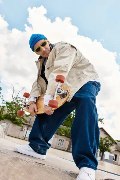 A young man in a stylish outfit skillfully holds his skateboard while standing in a park. — Stock Photo