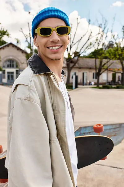 A cheerful young man enjoys the sunny weather in the park with his skateboard. — Stock Photo