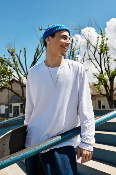 A cheerful young man stands outdoors in a park, casually leaning on his skateboard while smiling. — Stock Photo
