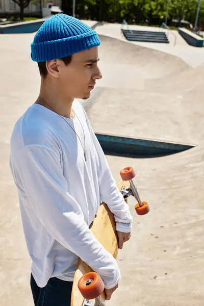 In a lively park, a young man stands with his skateboard, gazing thoughtfully into the distance. — Stock Photo