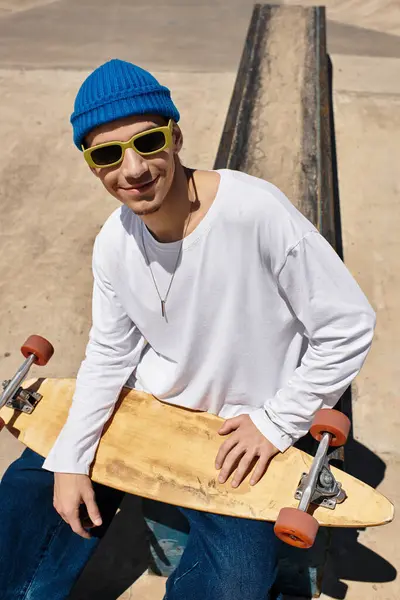 Bright day in the park as a young man with sunglasses sits confidently on his skateboard smiling. — Stock Photo