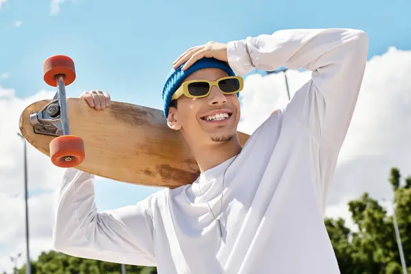 Joyful young man enjoys a sunny park day, confidently balancing a skateboard on his shoulder. — Stock Photo