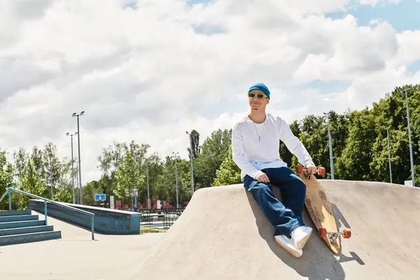 A young man with a skateboard relaxes on a ramp in a vibrant park, soaking in the sun and fresh air. — Stock Photo