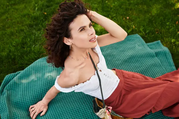 Young woman relaxes on a green picnic blanket, soaking up the sun in stylish summer outfit outdoors. — Stock Photo