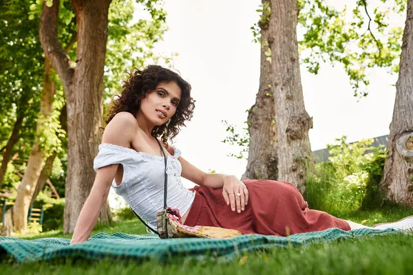Bright summer day finds a beautiful young woman relaxing on a blanket surrounded by trees — Stock Photo