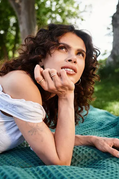 Una hermosa joven disfruta de un día soleado, acostada sobre una manta en el parque mientras admira la naturaleza. - foto de stock