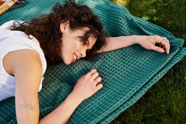 A beautiful young woman relaxes on a green blanket in a sunny park, enjoying nature and serenity. — Stock Photo