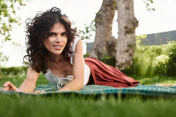 Young woman lies on a blanket in a lush park, embracing the warmth of a sunny summer day. — Stock Photo