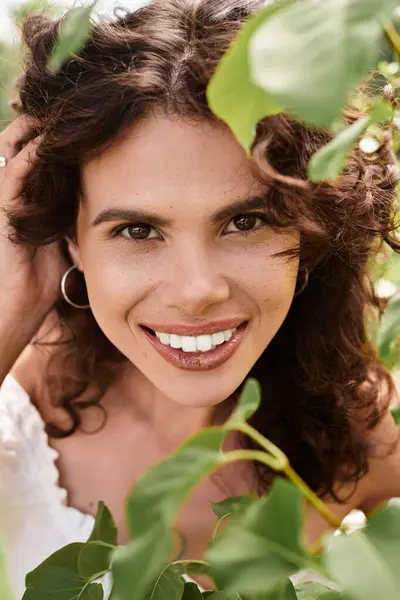 Young woman smiles radiantly while surrounded by vibrant green leaves, embodying summer joy. — Stock Photo
