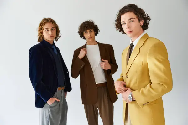 Trois jeunes hommes vêtus de tenues branchées posent ensemble dans un studio bien éclairé. — Stock Photo