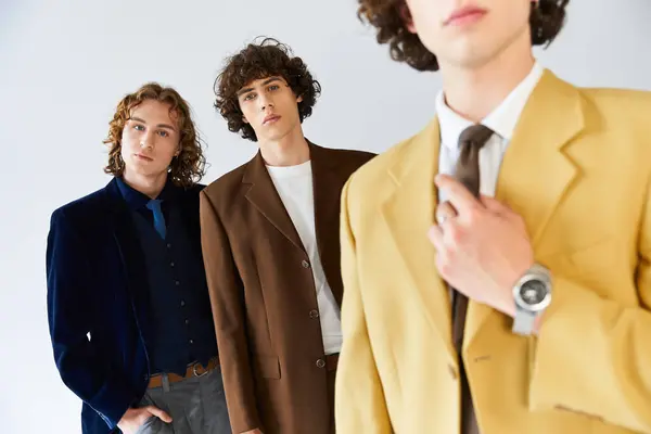 Trois jeunes hommes exposent leurs tenues branchées et posent avec confiance dans un studio élégant. — Stock Photo