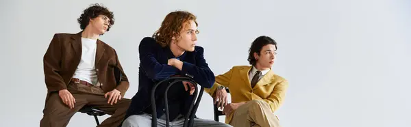 Three young men, each dressed in unique outfits, strike fashionable poses together in a studio. — Stock Photo