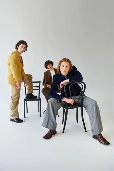 Trois jeunes hommes présentent leurs styles de mode tout en posant en toute confiance avec des chaises. — Stock Photo