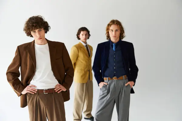 Three stylishly dressed young men stand together, each with unique fashion in a vibrant setting. — Stock Photo