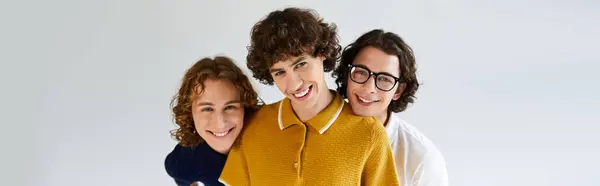 Three young men with trendy hairstyles and outfits stand closely, laughing while posing together. — Stock Photo