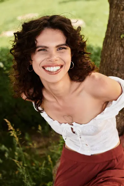 Una joven alegre sonríe brillantemente, rodeada de exuberante vegetación en un cálido día de verano. - foto de stock