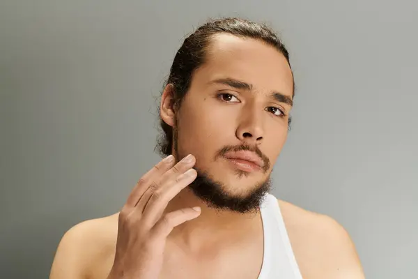 A young man with a beard touches his chin, exuding charm and confidence in a soft lit setting. — Stock Photo