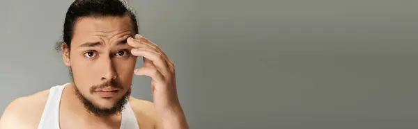 A young bearded man appears deep in thought while lightly touching his forehead, exuding charm. — Stock Photo