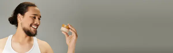 Young man with a beard smiles while examining a wellness product, radiating confidence and joy. — Stock Photo