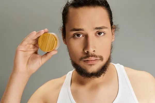Confident young man with a beard presents skincare product while posing against a neutral background — Stock Photo