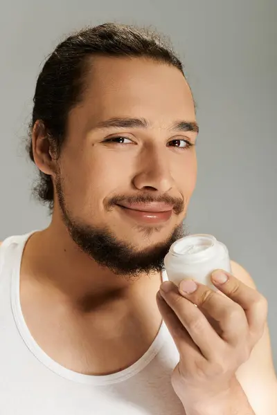 Young bearded man applies cream with joy in a bright indoor environment, radiating confidence. — Stock Photo
