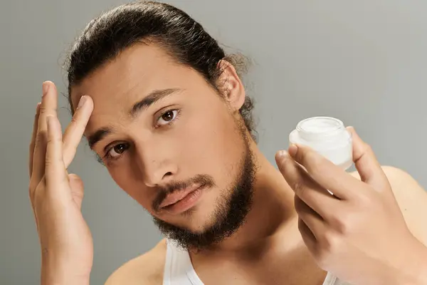 A handsome young man with a beard applies skincare while looking thoughtful in a stylish setting. — Stock Photo