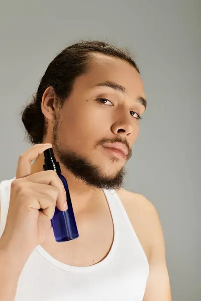 Young man with a beard uses a grooming spray while posing against a neutral backdrop of soft light. — Stock Photo
