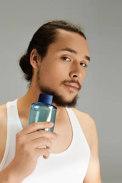 Young man with a beard confidently holding a grooming product against a neutral backdrop. — Stock Photo