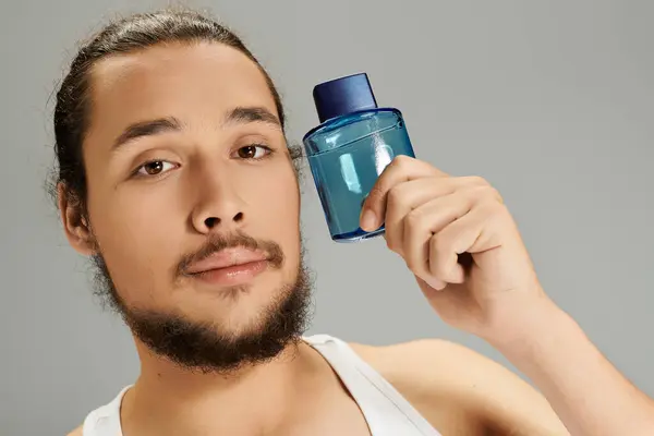 Handsome young man with a beard presents a vibrant cologne bottle while posing confidently. — Stock Photo