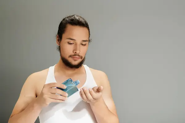 Young bearded man expertly dabs fragrance on his hand, exuding charisma in a minimalistic space. — Stock Photo