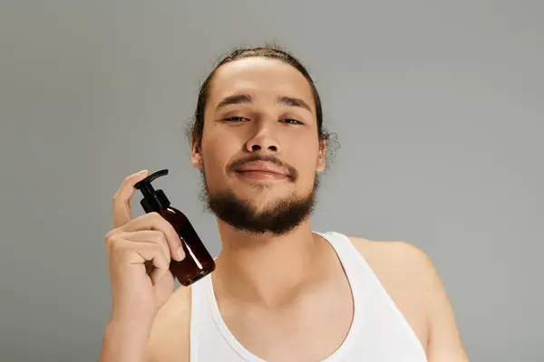 Young man with a charming beard smiles while holding a grooming product, exuding confidence. — Stock Photo