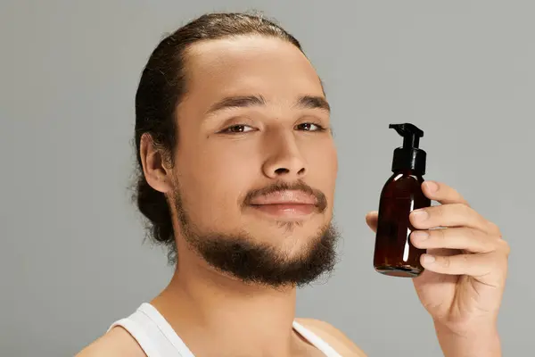 Charming young bearded man holds grooming product, showcasing his style and self care routine. — Stock Photo