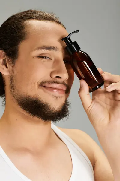 Young man with a beard holds a grooming product while smiling confidently in a studio environment. — Stock Photo