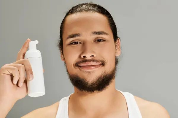 Young bearded man stands confidently, showcasing a skincare product with a friendly smile. — Stock Photo